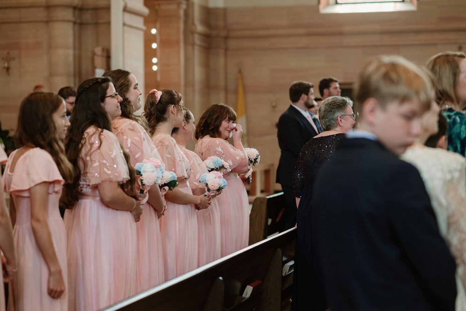 Wedding party members in formal attire stand in a line inside an elegant venue with pink and black color scheme.