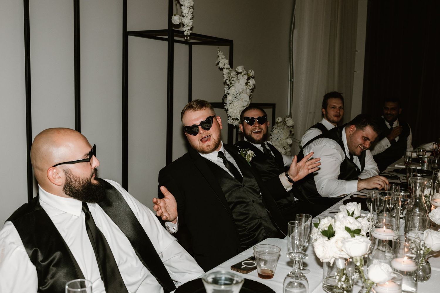 Wedding guests in formal attire enjoying conversation at a candlelit reception dinner table.