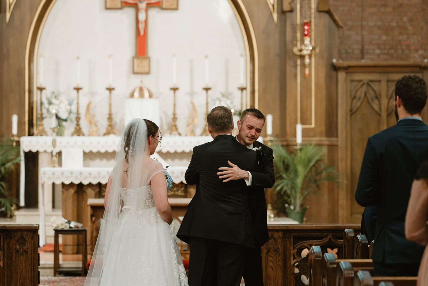 A romantic wedding ceremony takes place in an ornate church with wooden pews and a vaulted ceiling glowing with light.