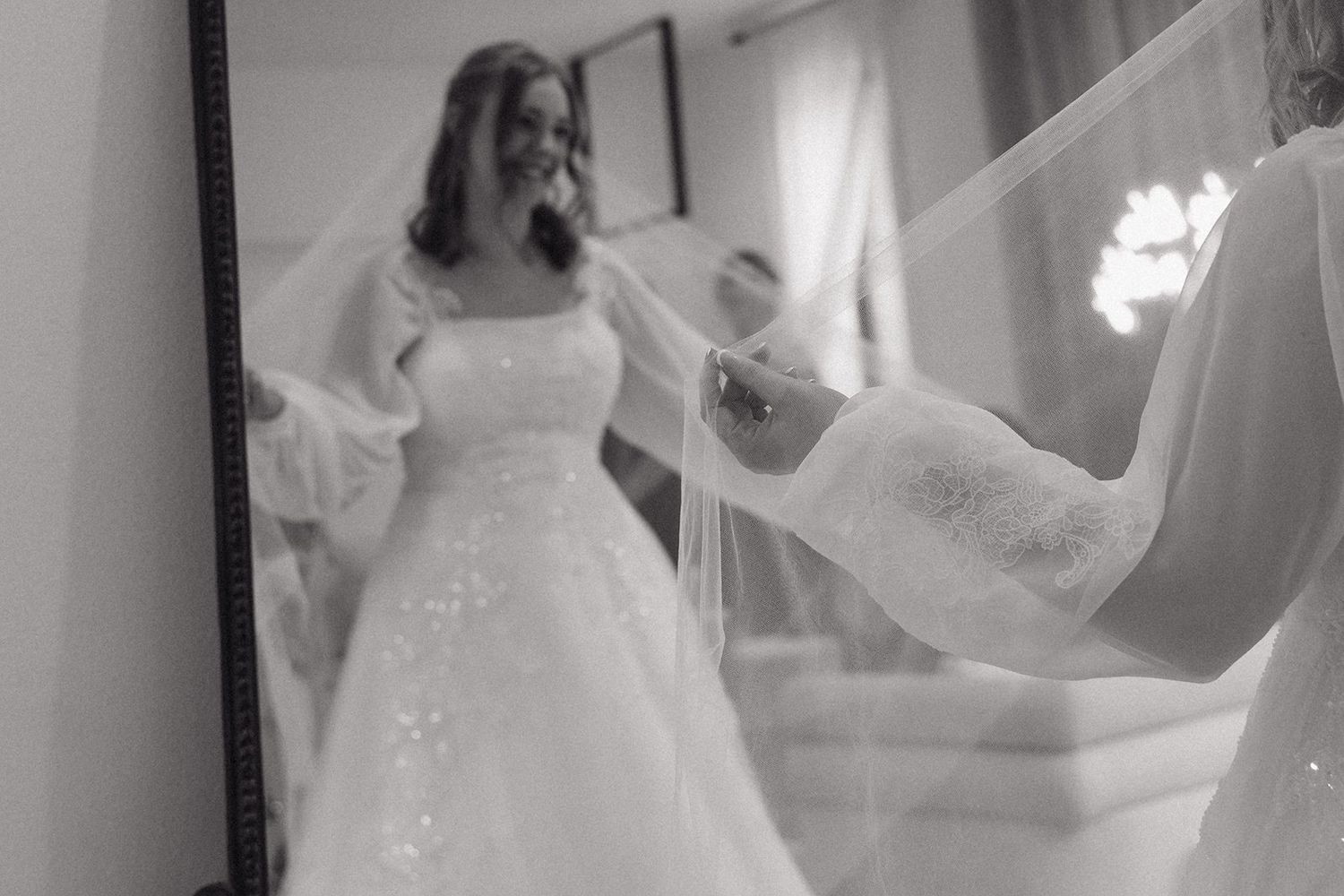 A bride in a white wedding dress twirls joyfully in front of a window, creating a romantic silhouette effect.