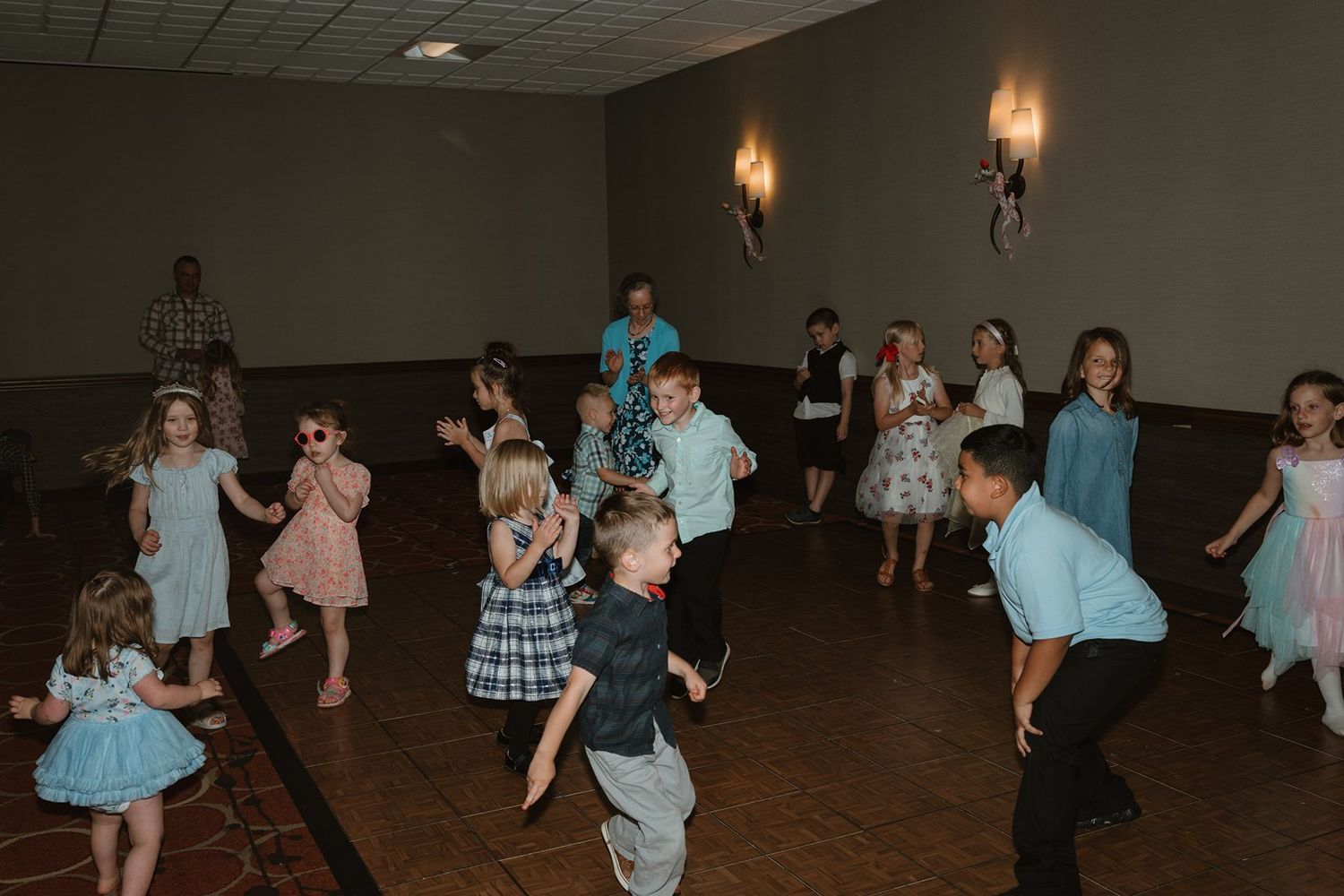 People in blue and black outfits dance together in a dimly lit ballroom with vintage wall sconces.