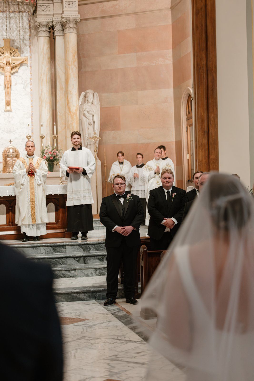 Traditional Catholic wedding ceremony taking place inside ornate church with clergy and altar servers on marble steps.