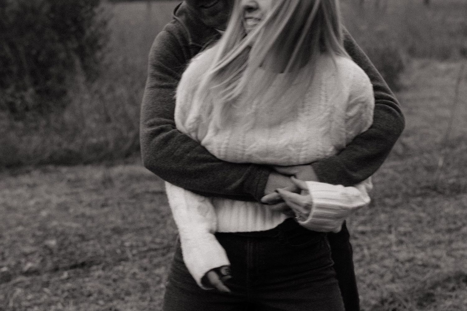 Black and white photo of two people sharing a warm embrace outdoors in a grassy field.