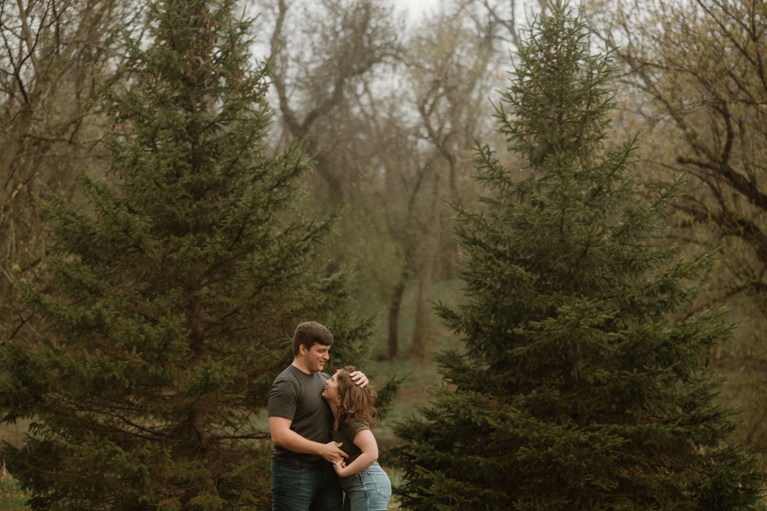 A romantic moment between a couple surrounded by evergreen trees in a moody, misty forest setting.