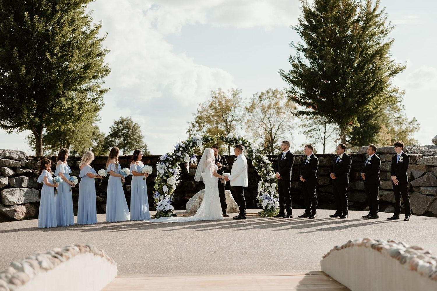Wedding party lined up during outdoor ceremony with blue and black formal attire.