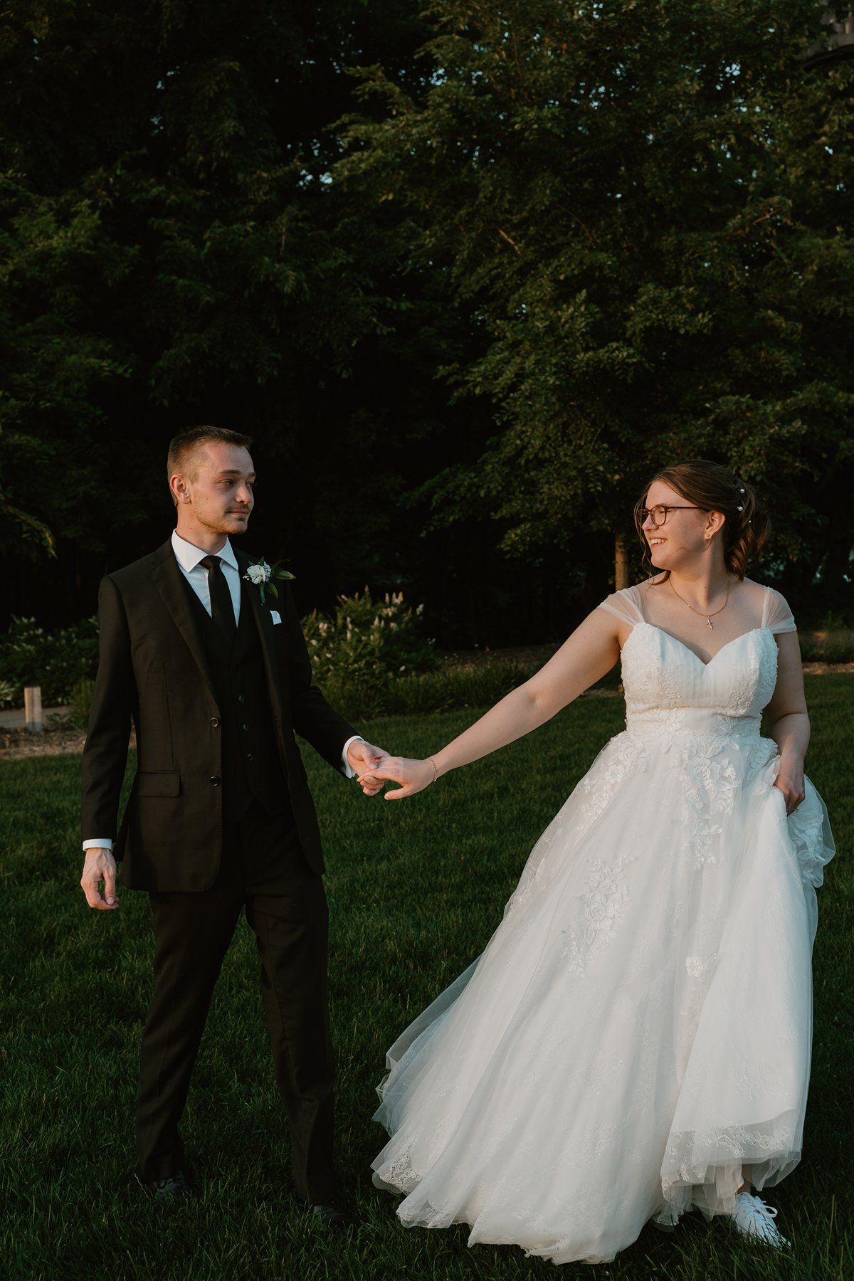A couple in wedding attire share a playful moment among trees in a natural outdoor setting.