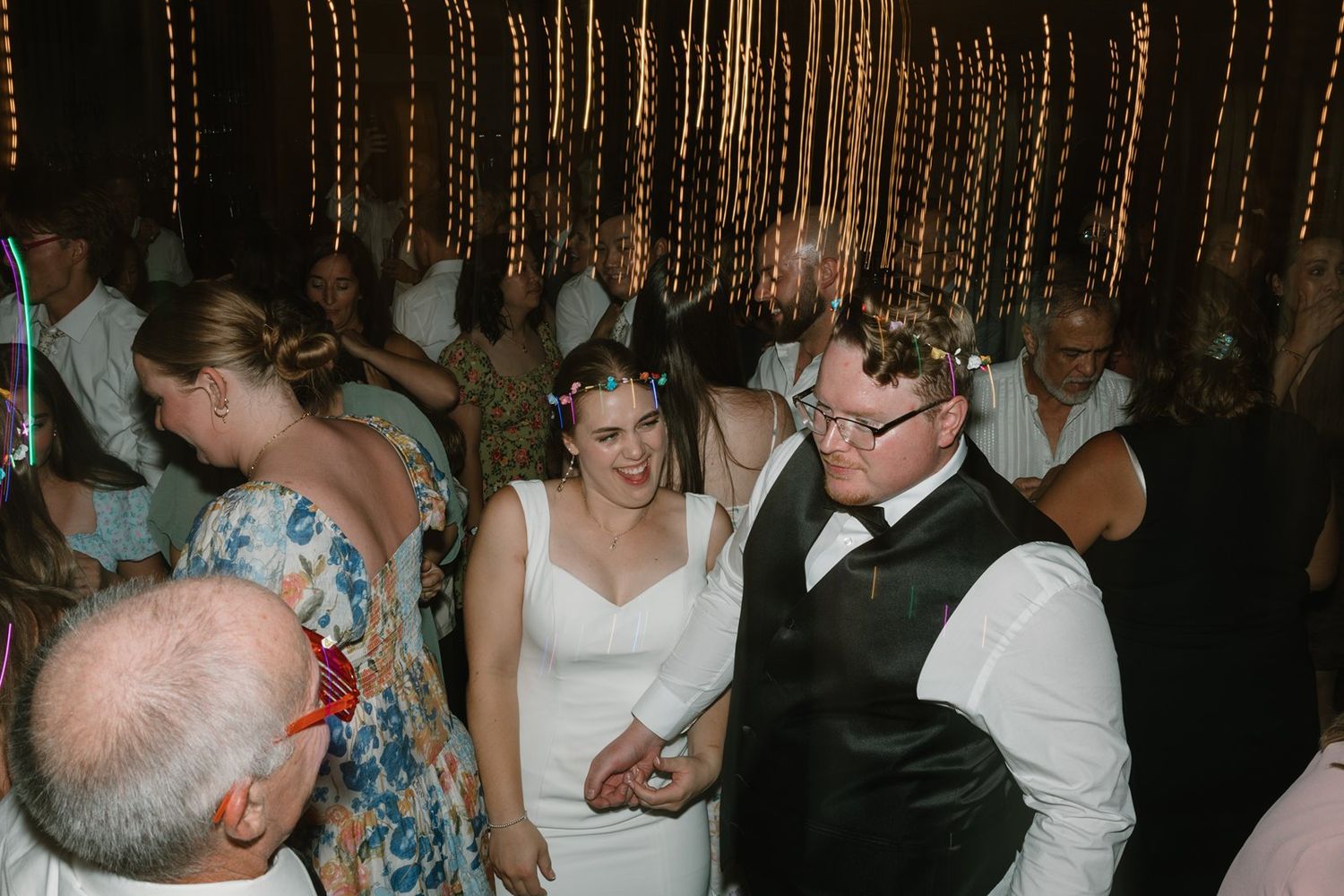 Wedding guests enjoying themselves on a crowded dance floor with string lights overhead.