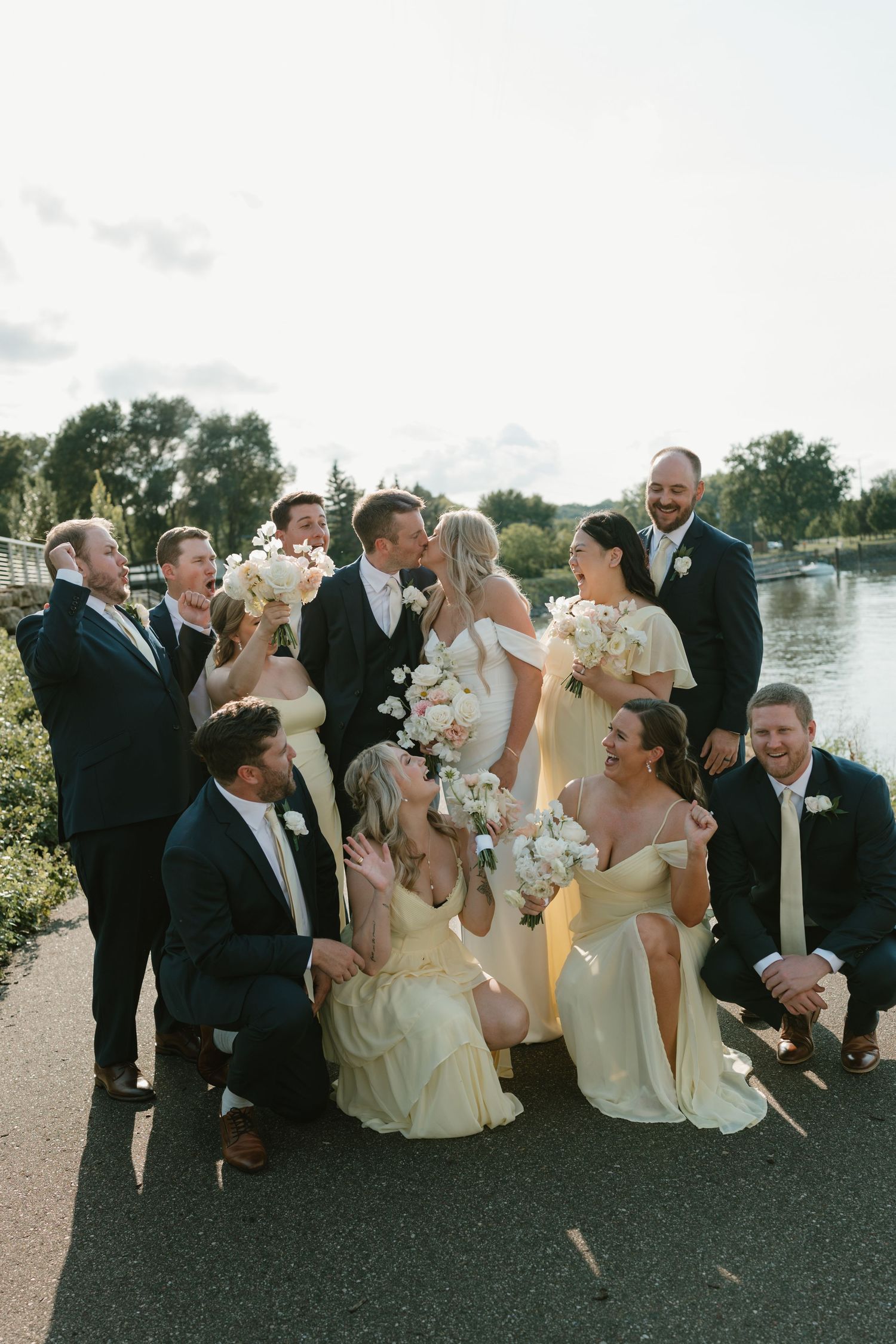 Wedding party poses playfully together outdoors by a lake during sunset celebration.