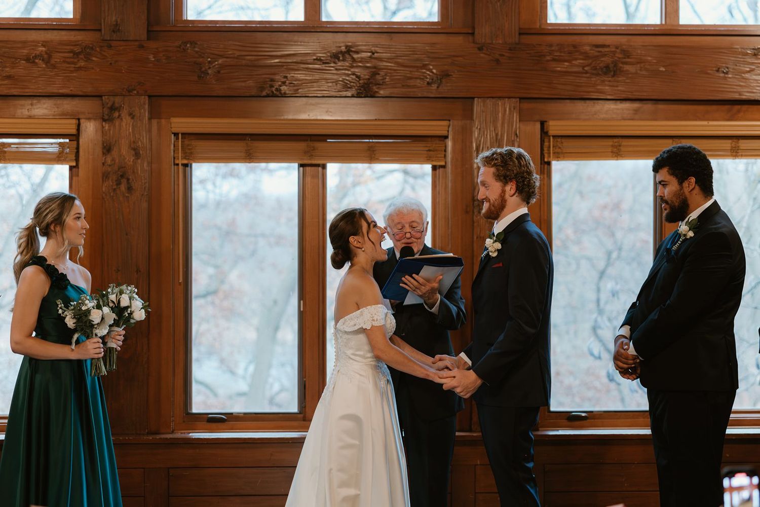 Wedding ceremony takes place in a rustic wood-paneled room with large windows.