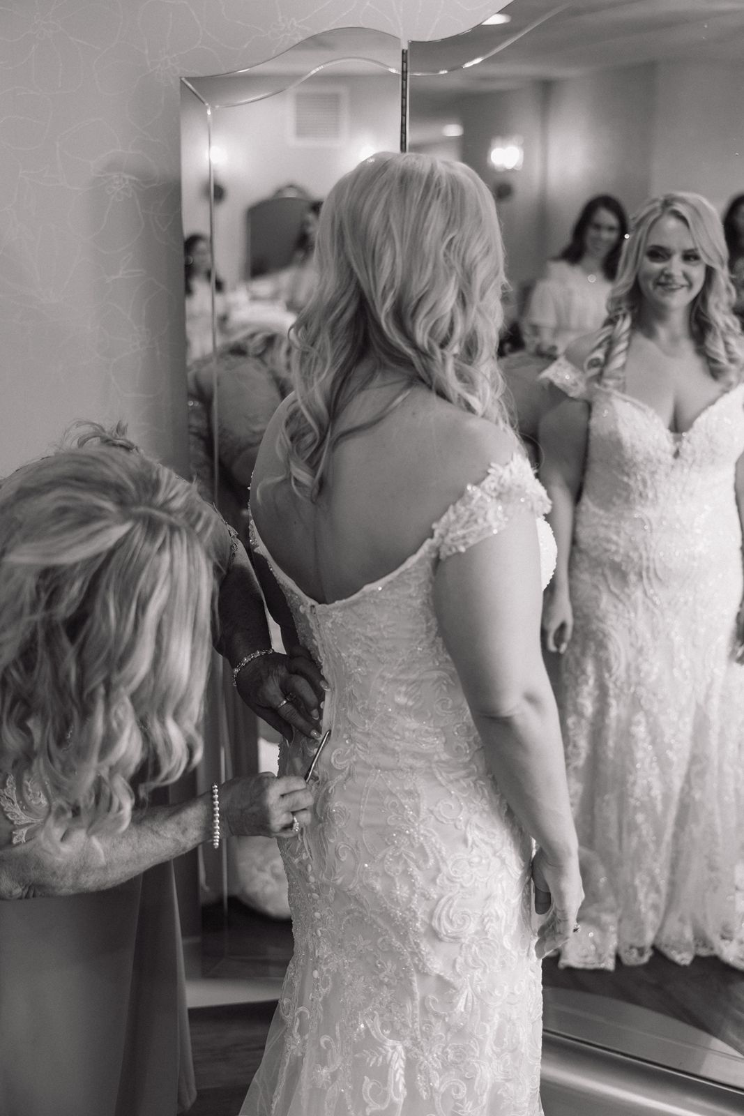 A bride in a lace gown looking at her reflection while getting ready.