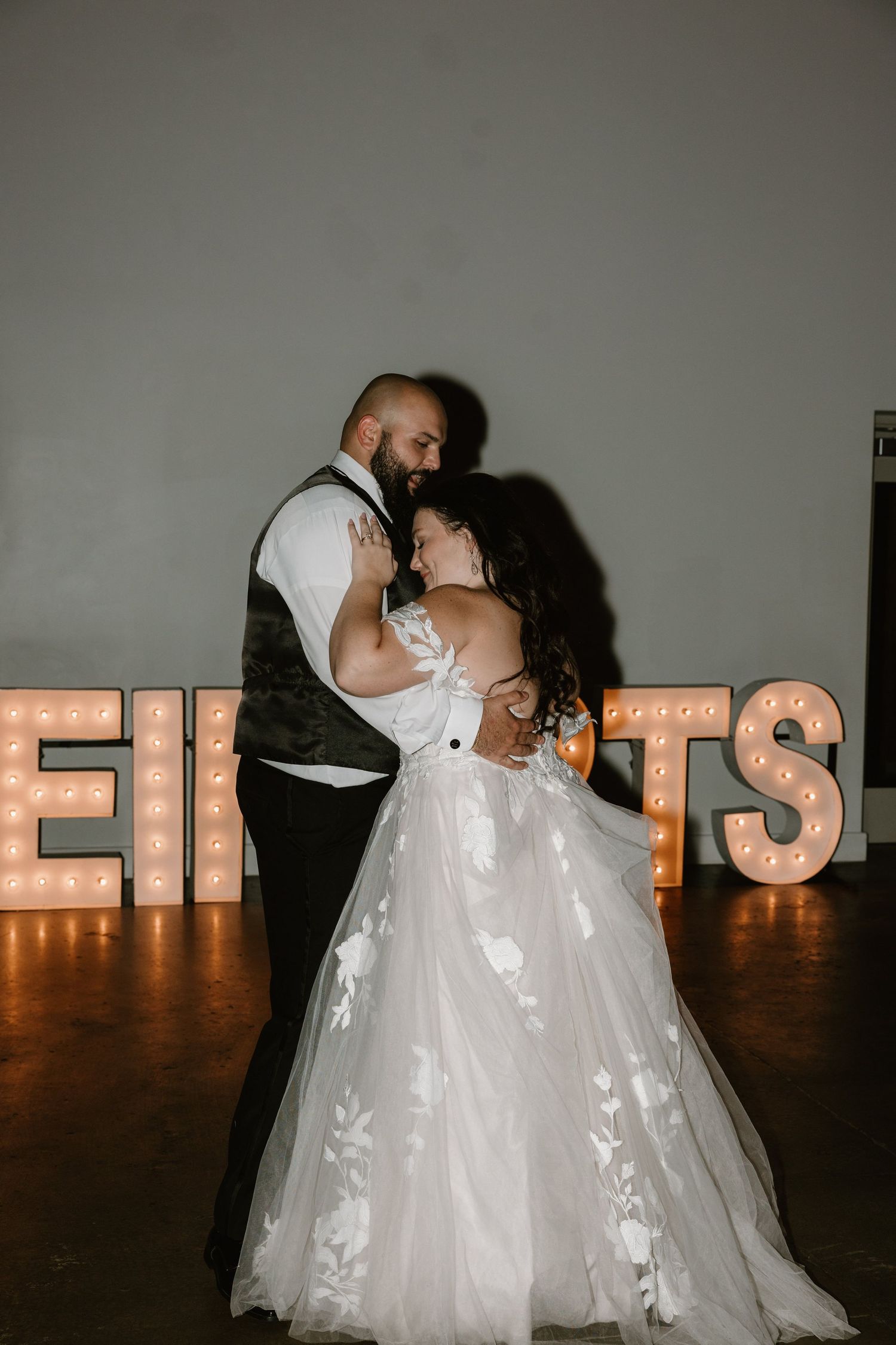 A romantic wedding couple shares an intimate dance moment in front of illuminated marquee letters spelling EIGHTS.