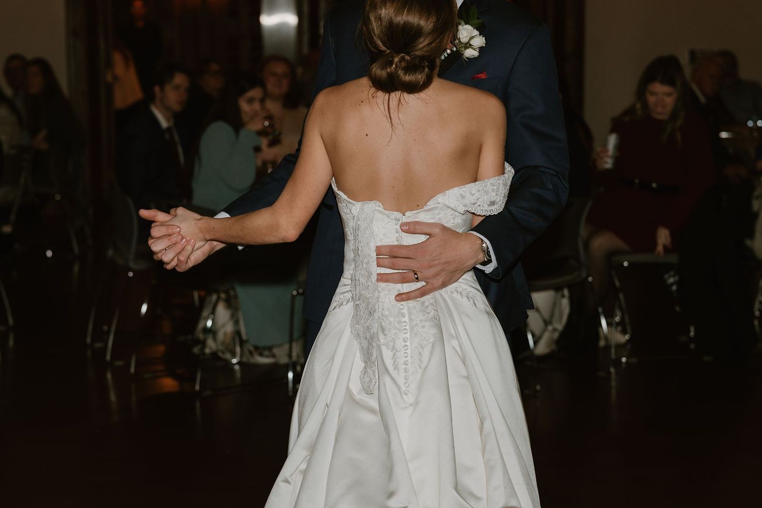 Close-up of couple's embrace during wedding dance showing detailed back of white gown.