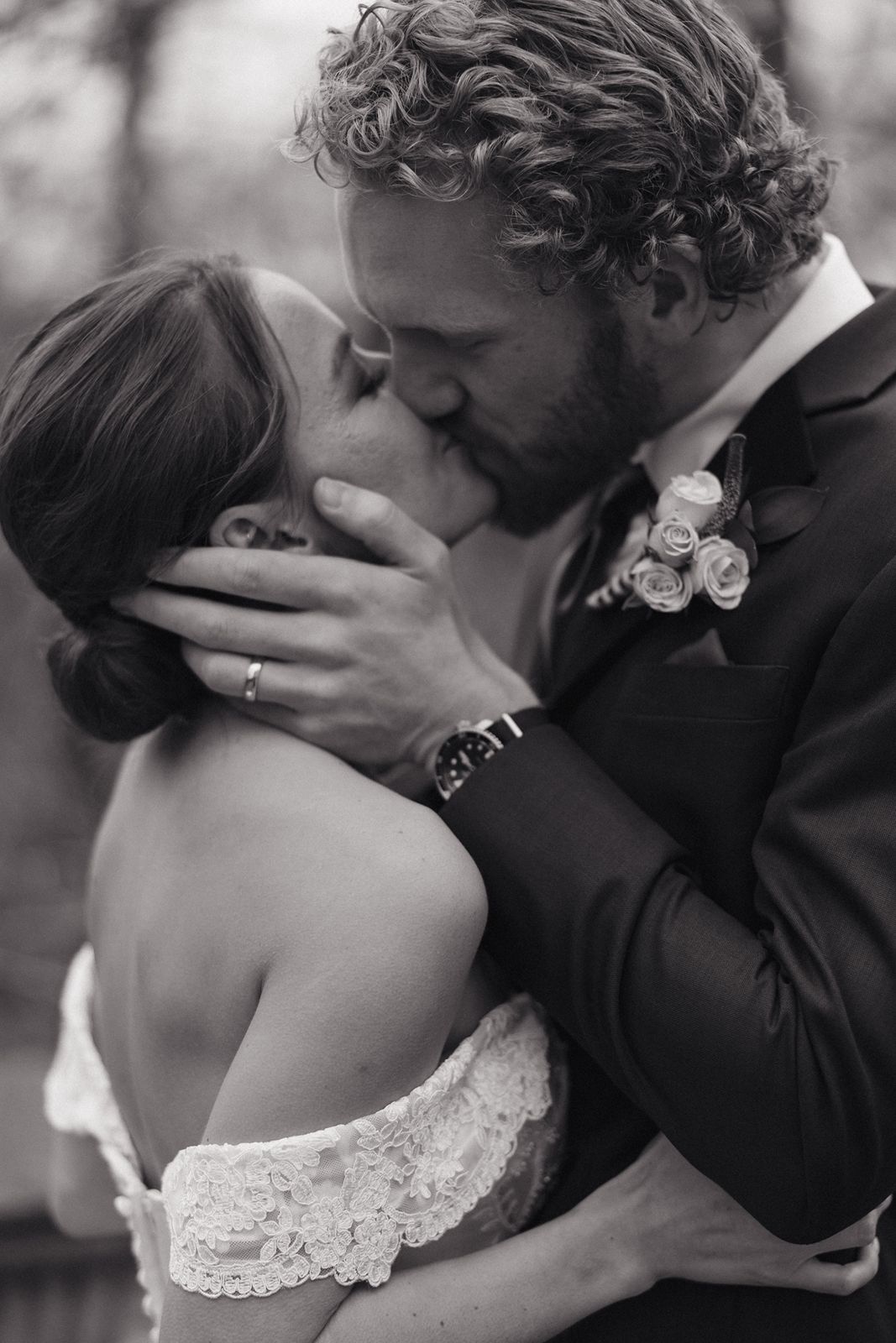 A romantic black and white wedding photo captures a tender kiss between newlyweds during their outdoor ceremony.