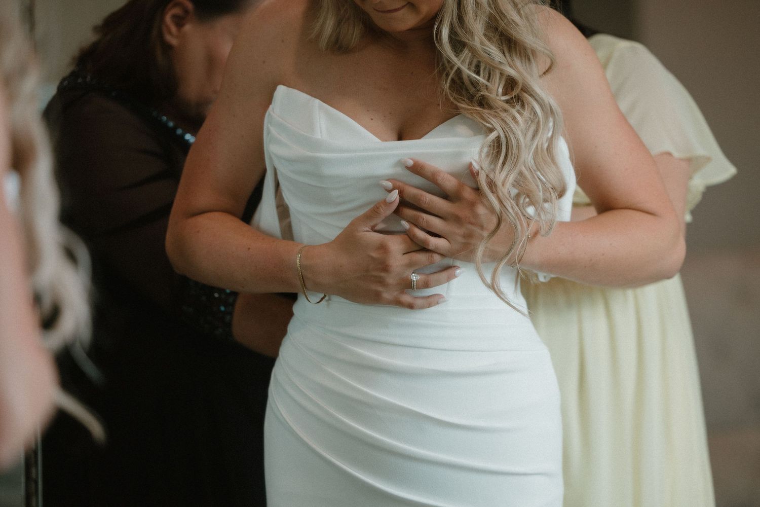 Close-up shot of hands helping to adjust a white strapless wedding dress on a bride.