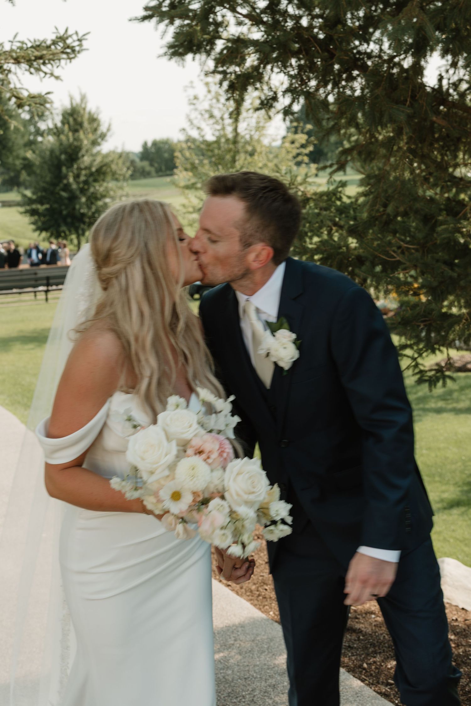 A romantic wedding couple shares a tender kiss outdoors surrounded by lush greenery on their special day.