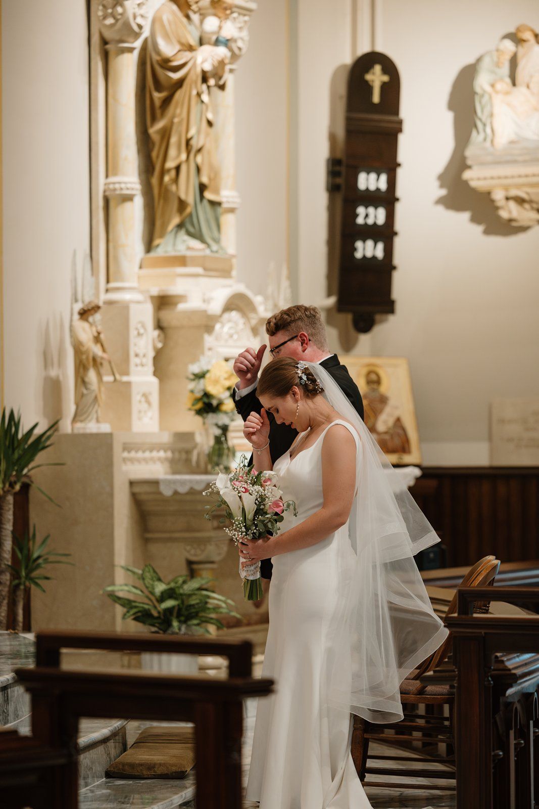 Bride in white dress and veil sharing emotional moments in church sanctuary.
