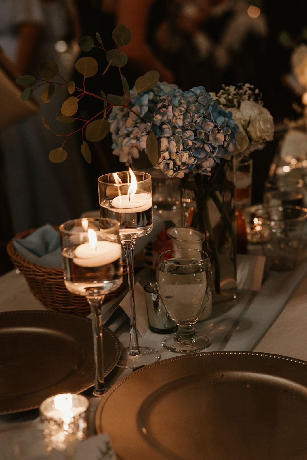 Elegant wedding table setting with lit candles, blue hydrangeas, and romantic evening ambiance.