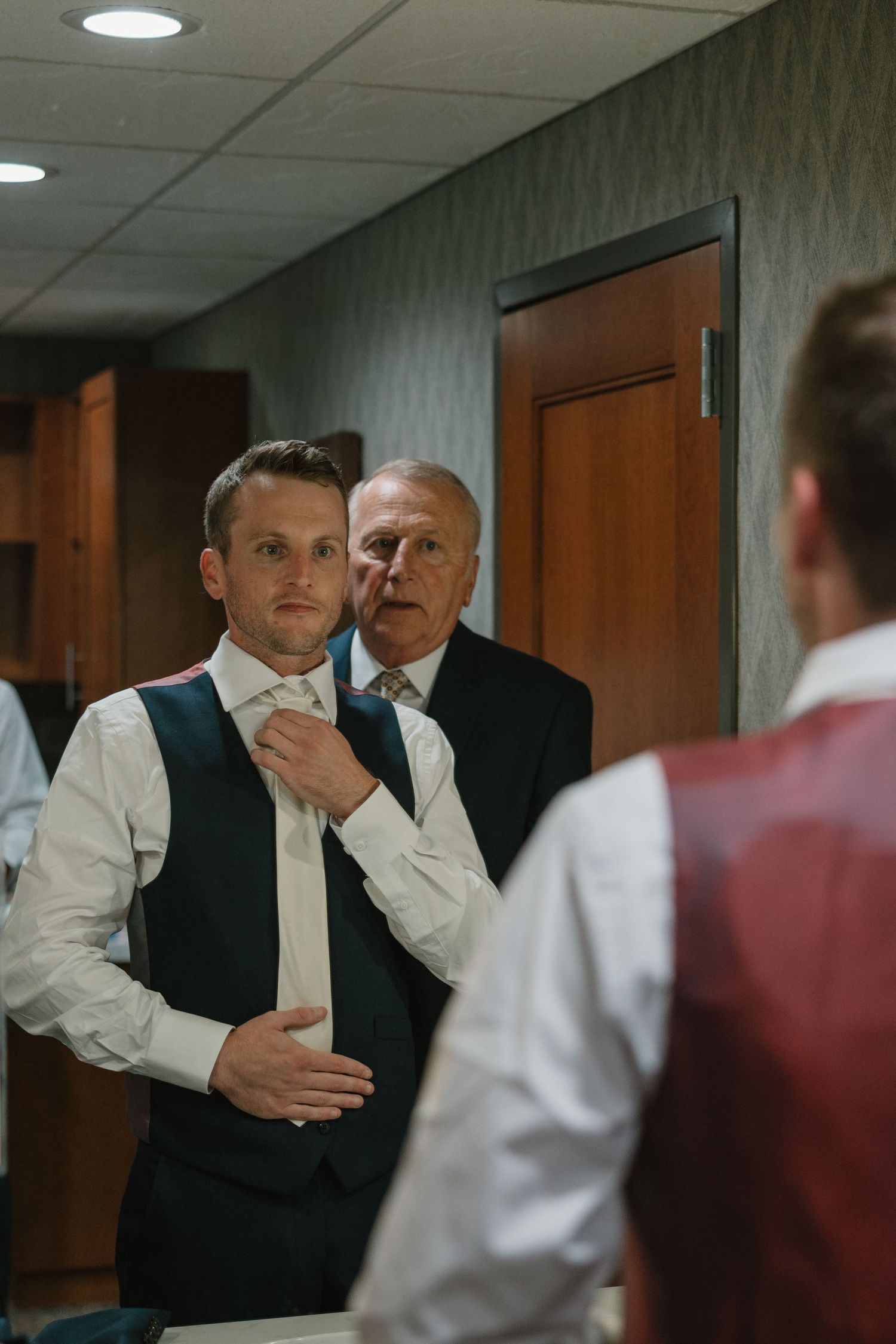 People in business attire having a discussion in an office hallway with fluorescent lighting and wooden doors.