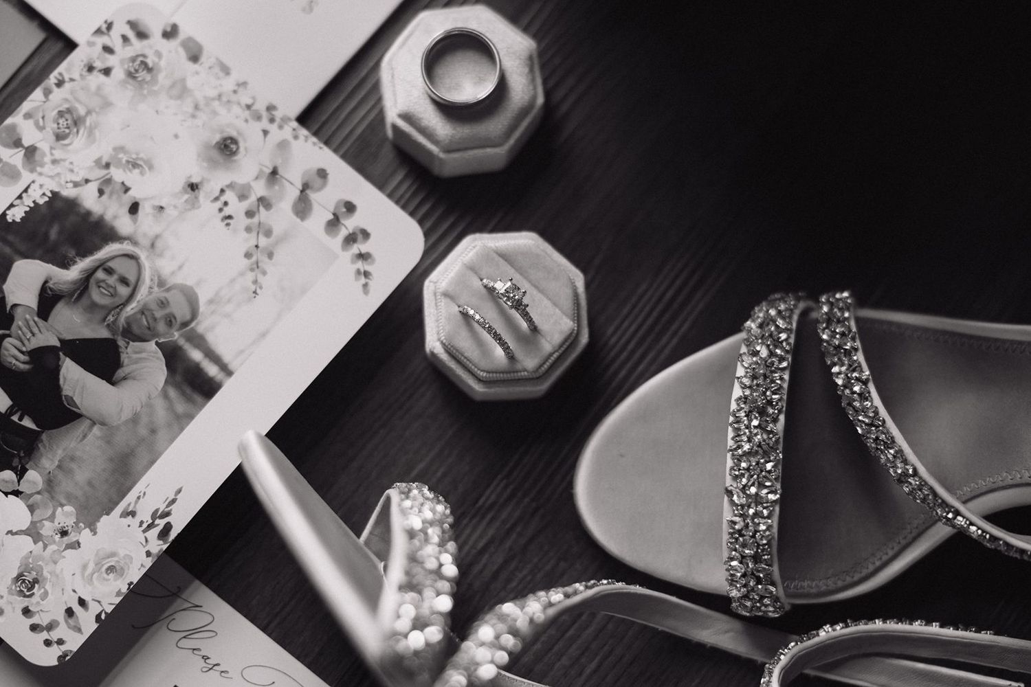 Wedding accessories including jewelry, shoes and photographs arranged on dark wood surface.