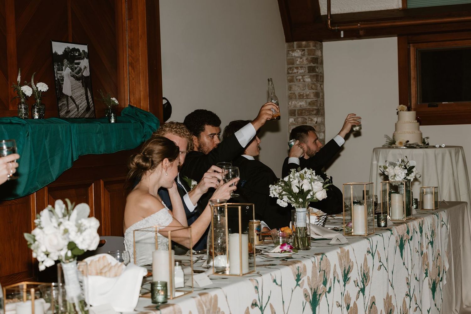 Wedding party celebrates with raised glasses at decorated head table.