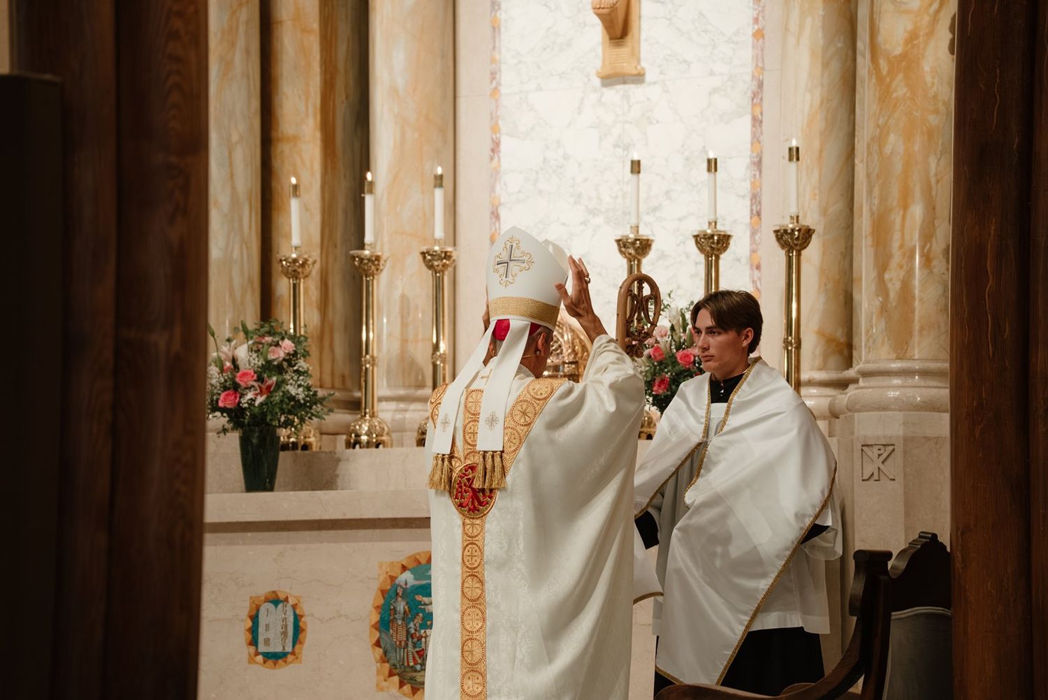Catholic priest performs religious ceremony at ornate church altar with candles and decorative elements.