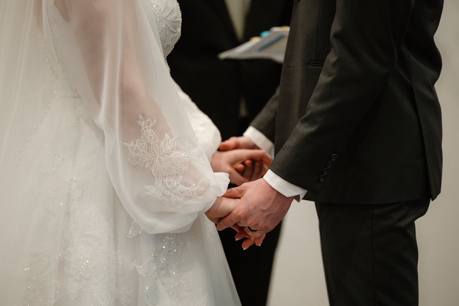 Close-up shot of hands holding during an elegant wedding ceremony in formal black and white attire.