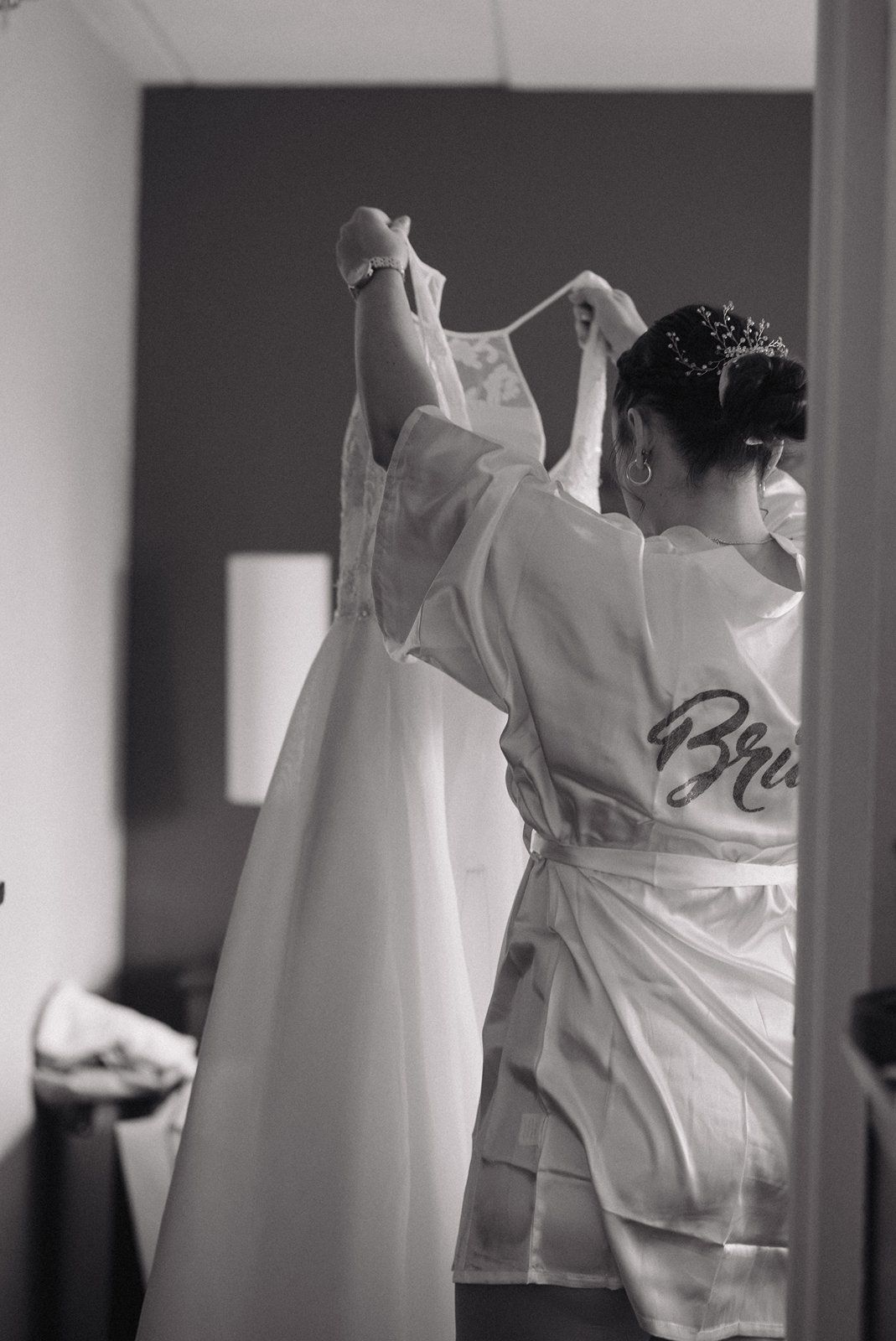 A black and white photo of someone in a white robe preparing a wedding dress during pre-wedding preparations.