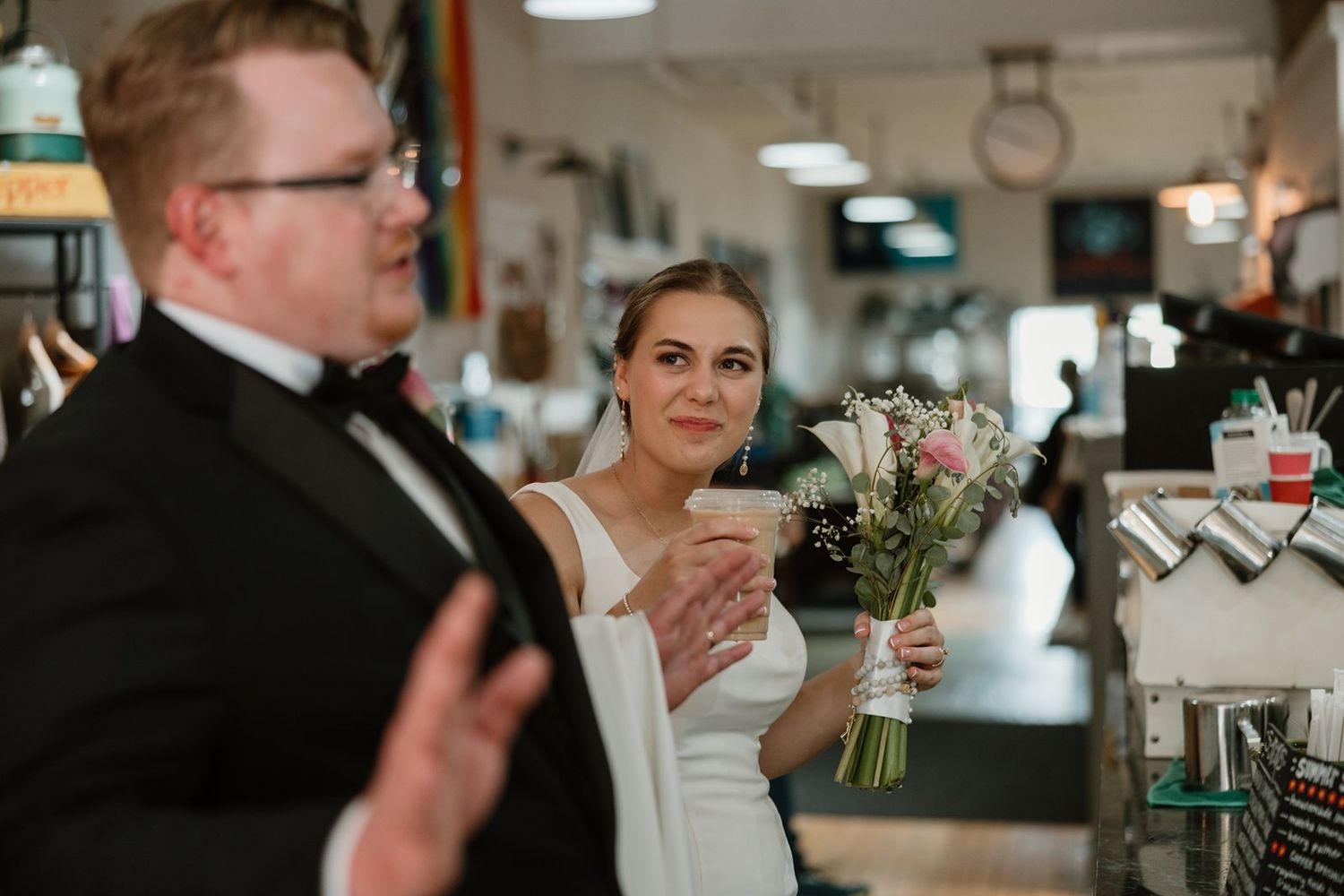 Wedding guests enjoy drinks and conversation at a lively indoor reception with warm lighting and floral decorations.