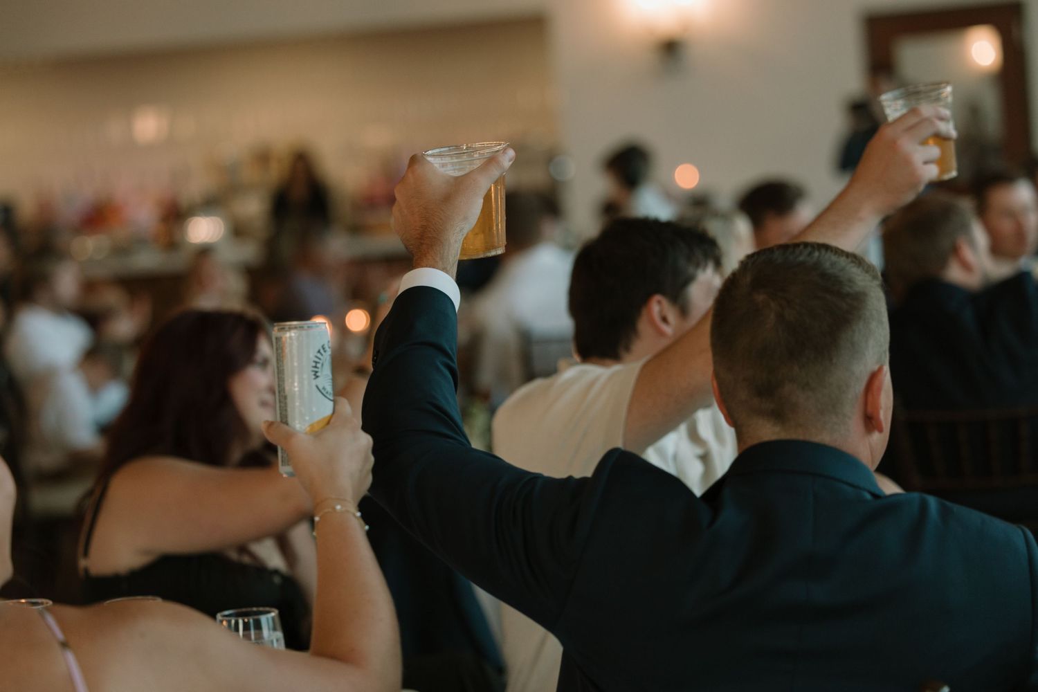 Wedding reception crowd scene with guests raising glasses in celebration.