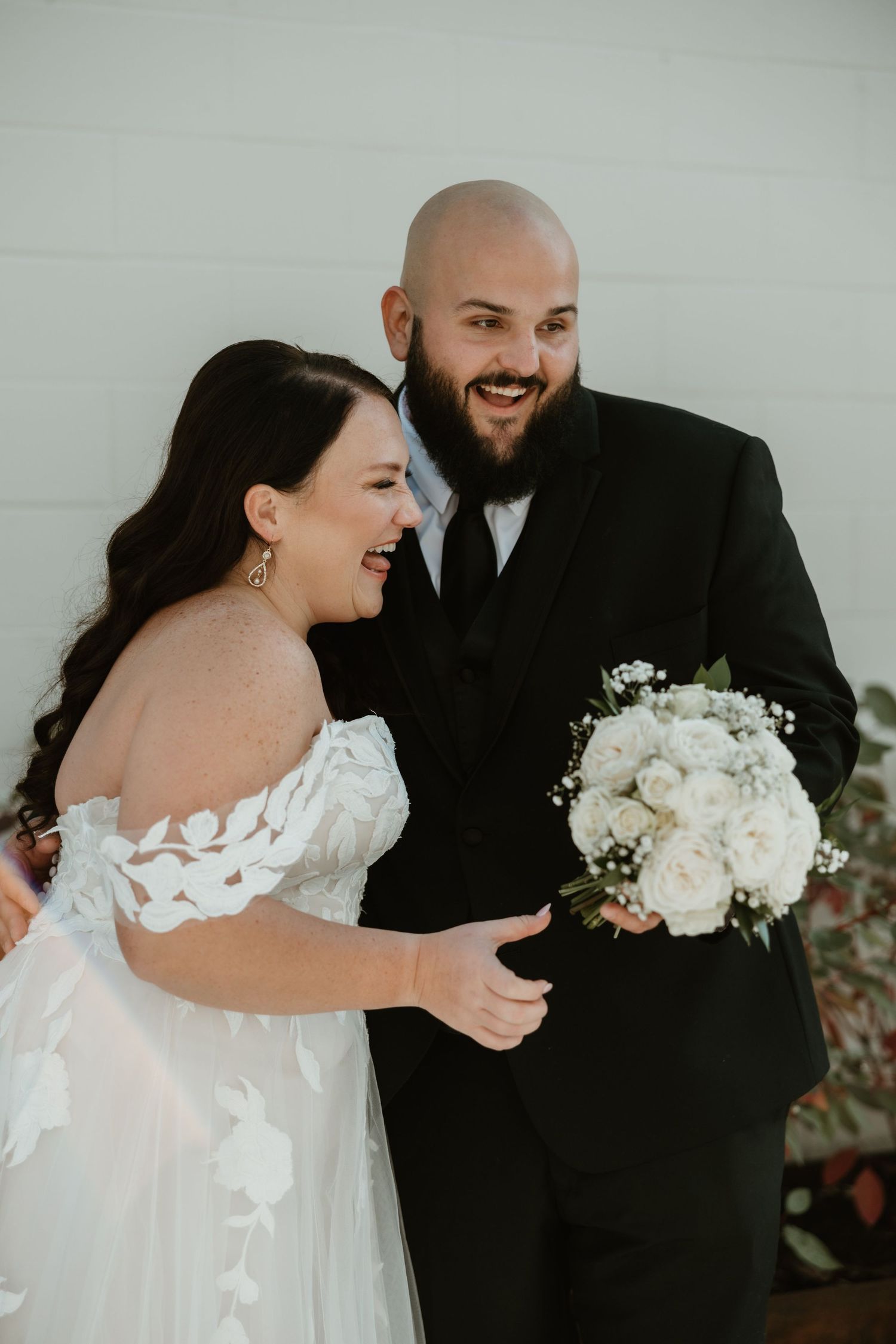 A happy couple shares a joyful moment during their wedding ceremony while holding a white rose bouquet.