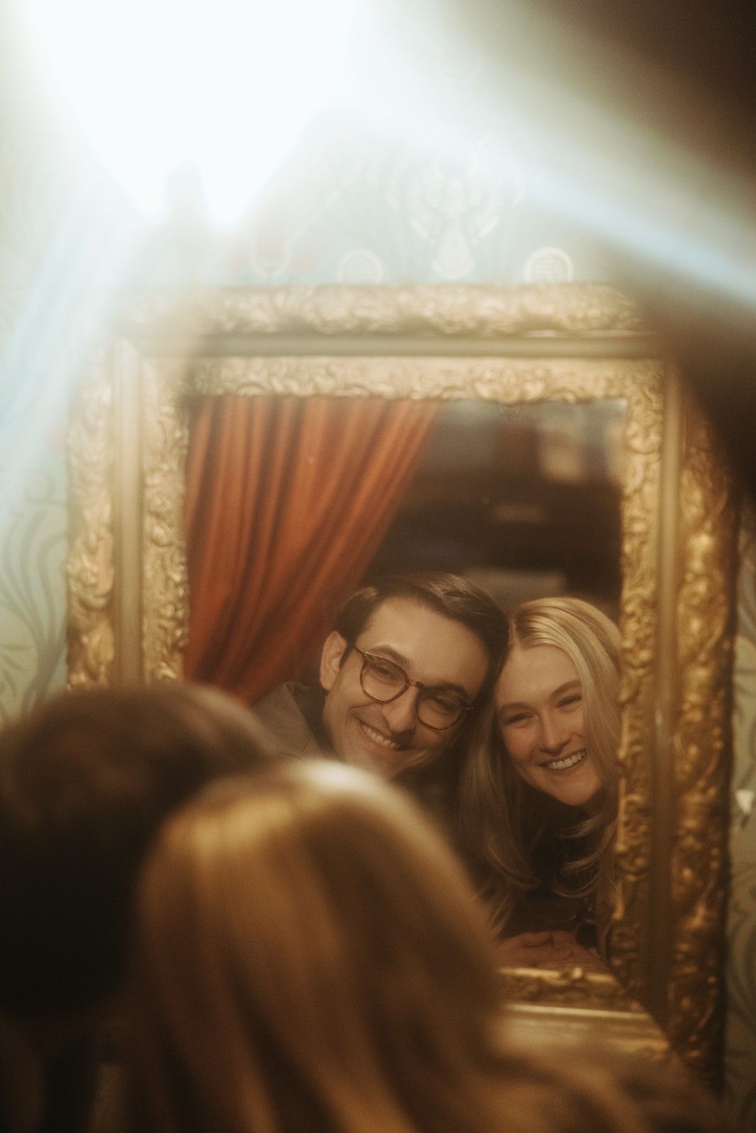 Reflection of couple smiling together in ornate gold mirror with dreamy soft focus lighting.