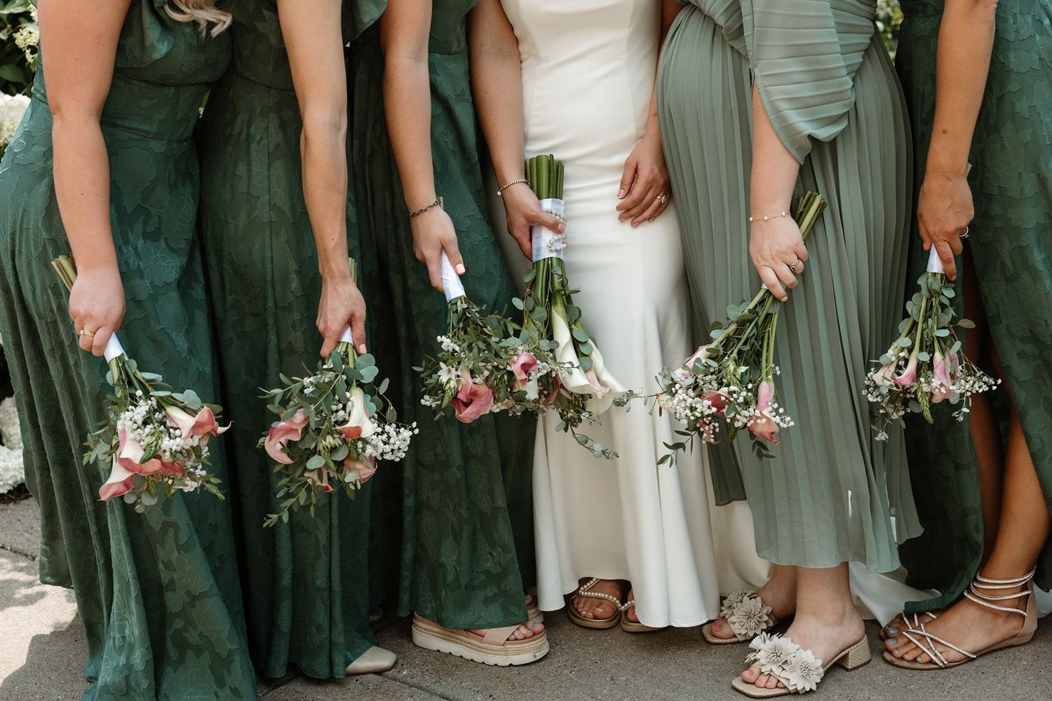 Row of bridesmaids in sage green dresses showing their shoes and bouquets.