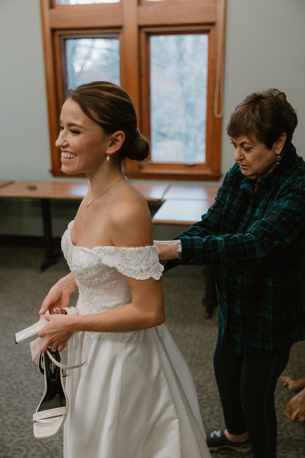 Beautiful off-shoulder wedding dress being adjusted by the bride's grandma in preparation for the ceremony.