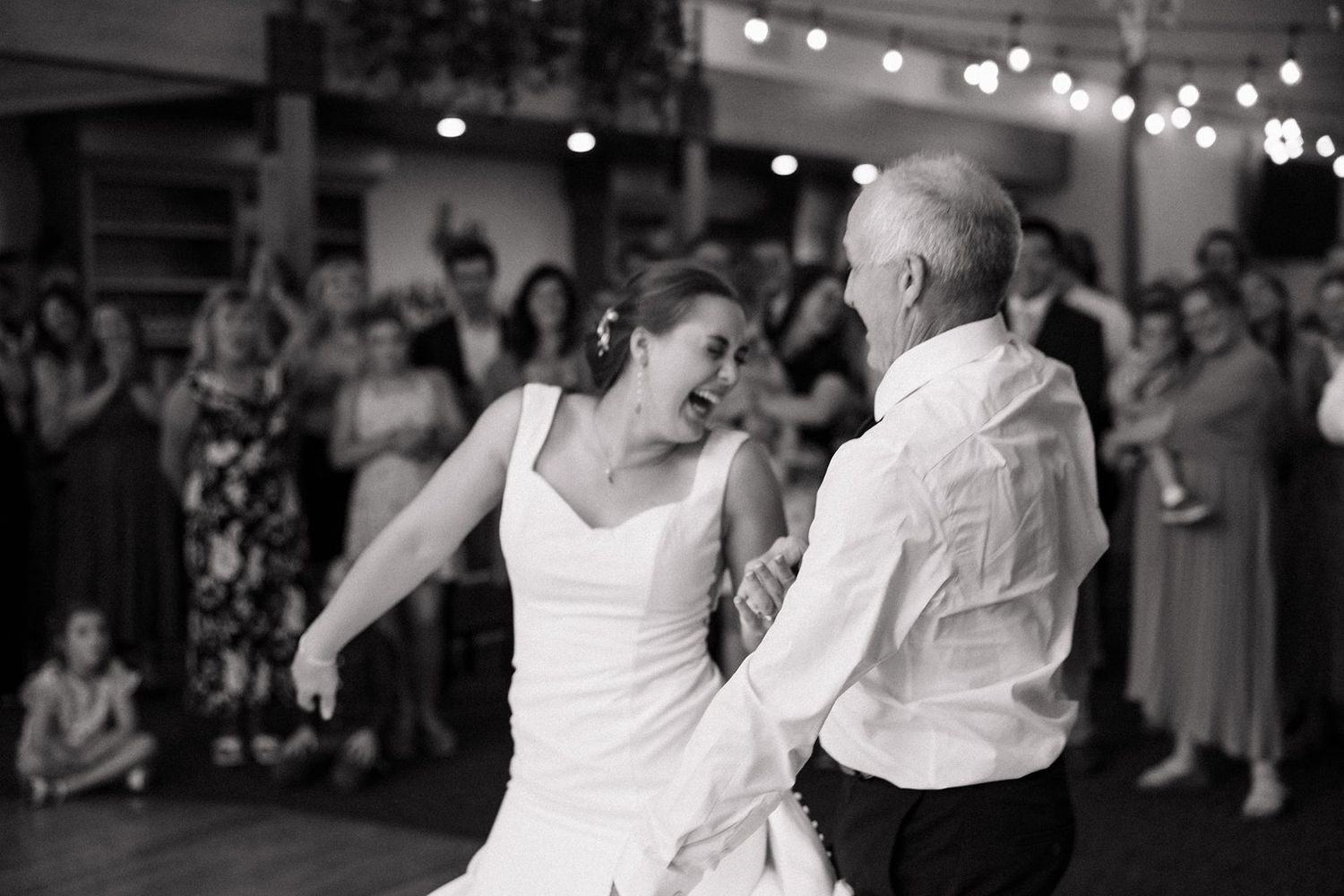 A couple shares a joyful dance moment at their wedding reception as guests watch in the background.