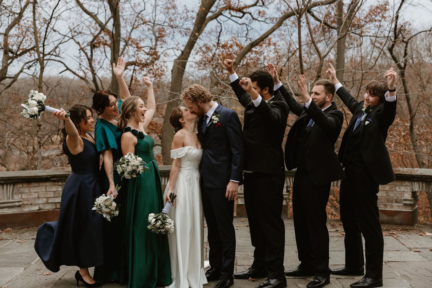 Wedding party poses together outdoors with bridesmaids in navy and emerald dresses.