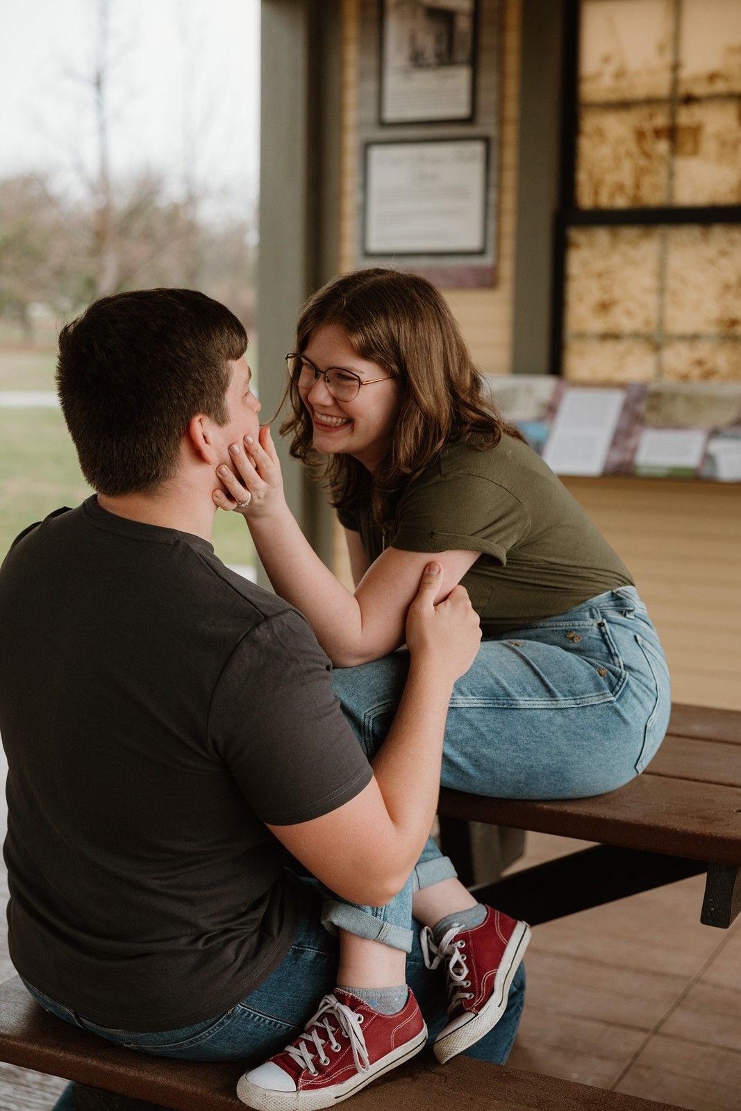 A couple shares an intimate moment while sitting together on a wooden bench on a covered porch.