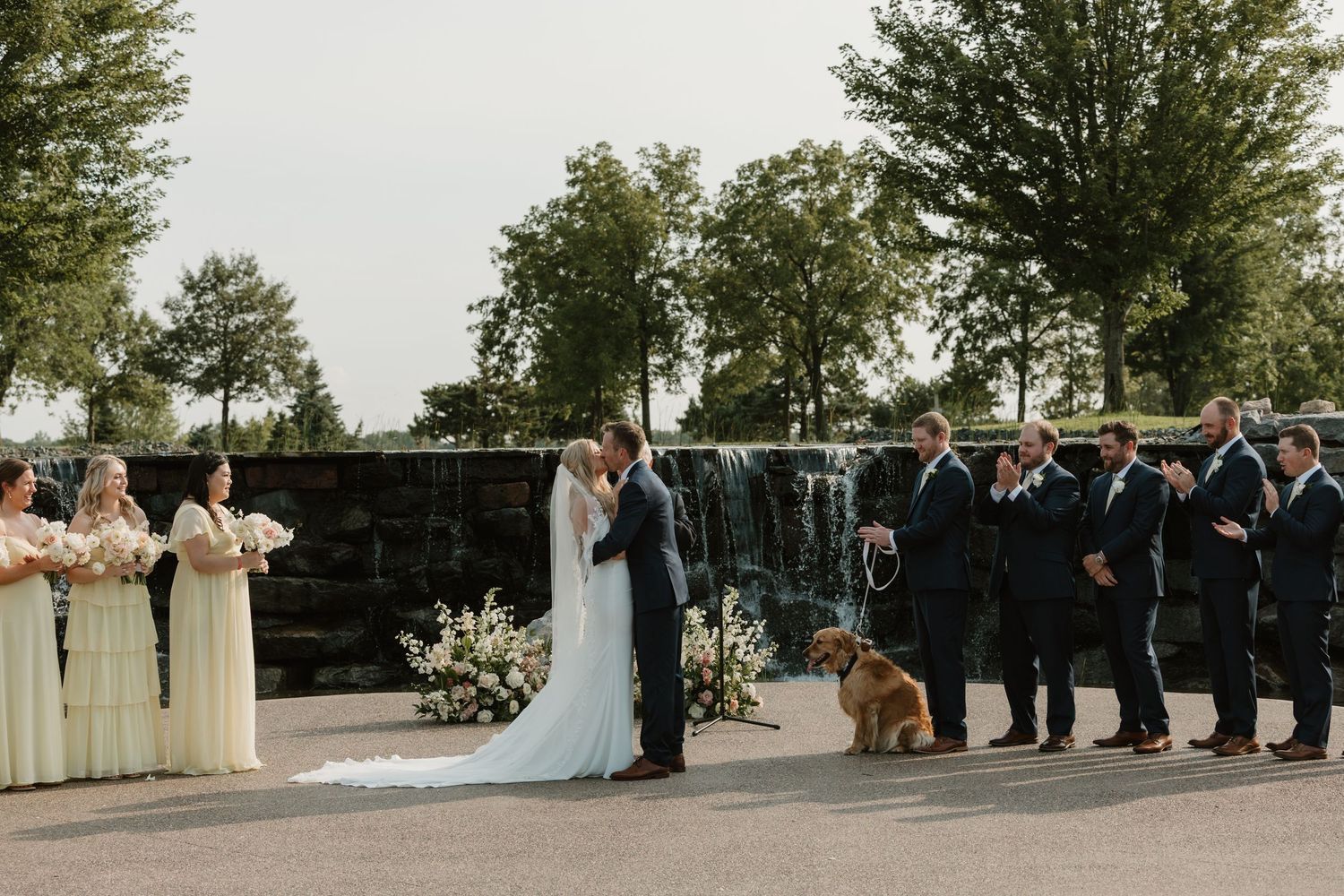 Outdoor wedding ceremony with wedding party and a brown dog sitting attentively by the altar.