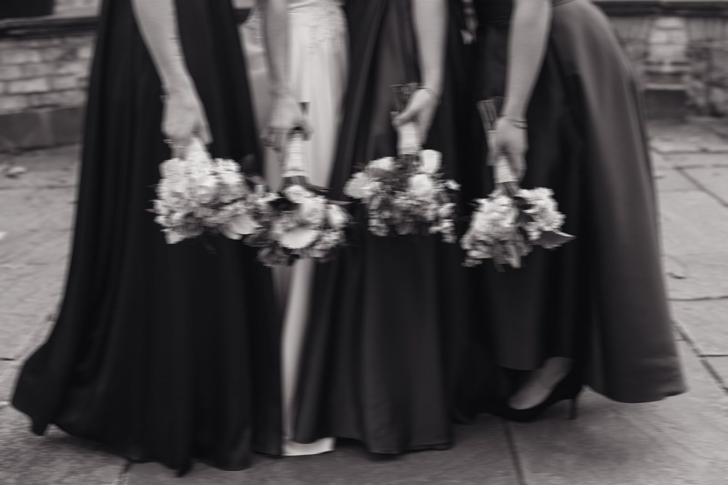 Black and white image of bridesmaids holding bouquets, showing the bottom of their formal dresses.