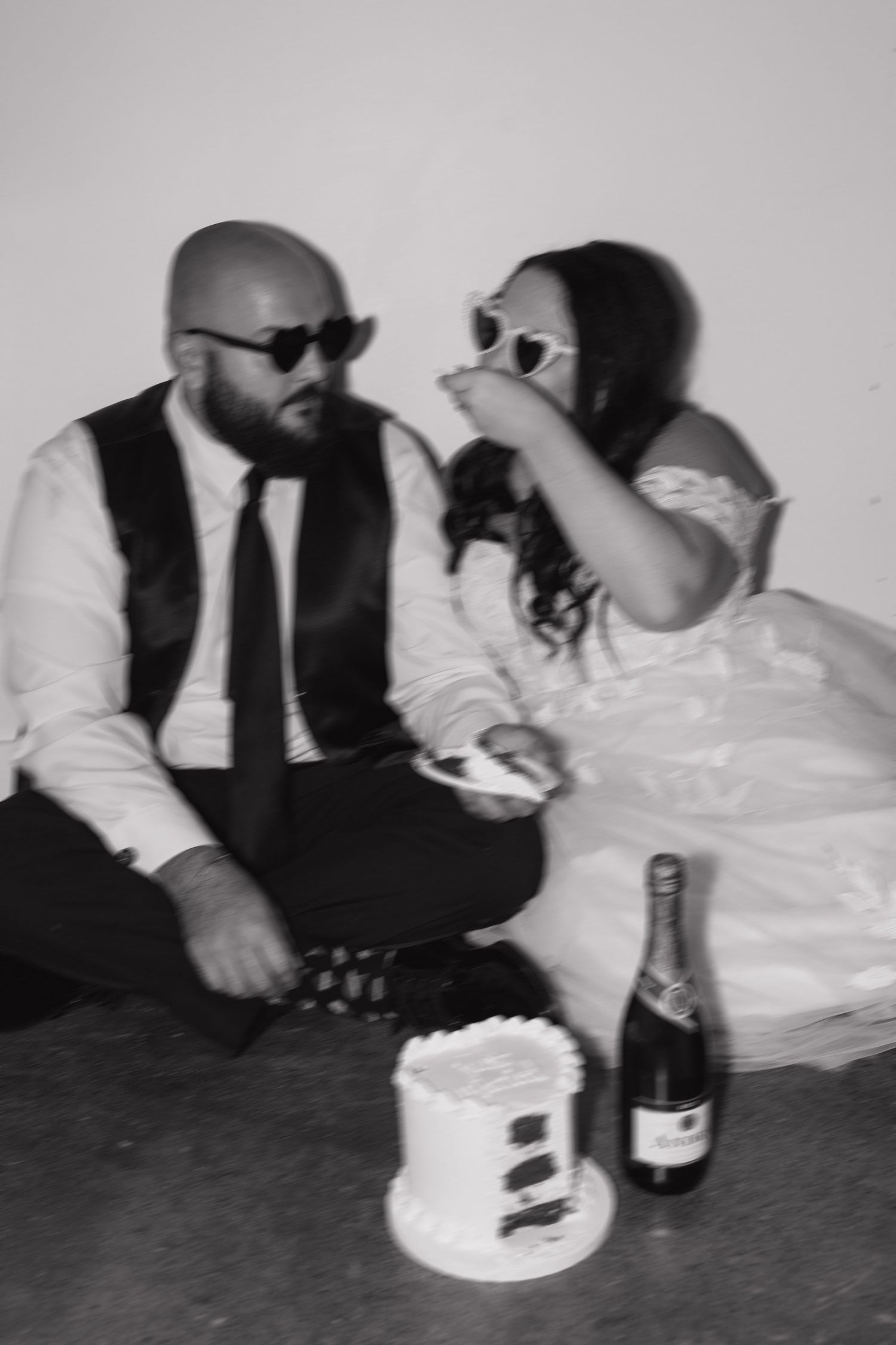 Black and white photo of a couple wearing sunglasses eating cake on the bathroom floor