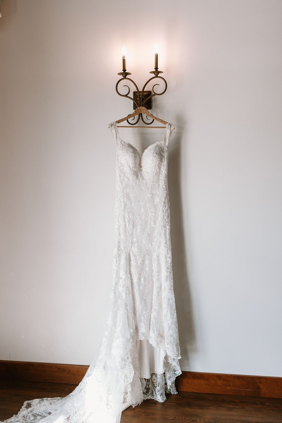 A classic lace wedding dress hanging from an ornate wall sconce with candles.