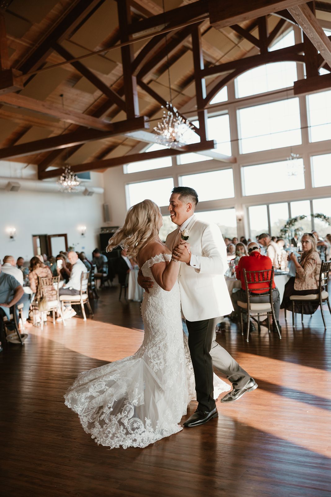 Couple shares their first dance in a rustic reception venue with wooden beams.
