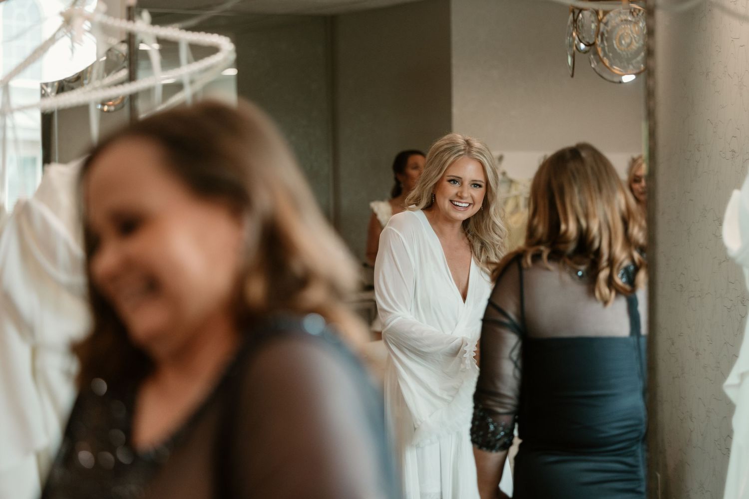 Bridesmaids in teal dresses help bride get ready in sunlit room before wedding ceremony.