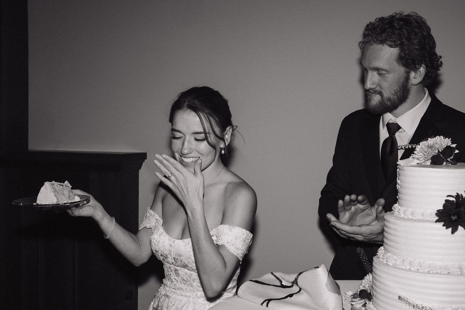 Black and white photo of couple enjoying cake during wedding reception.