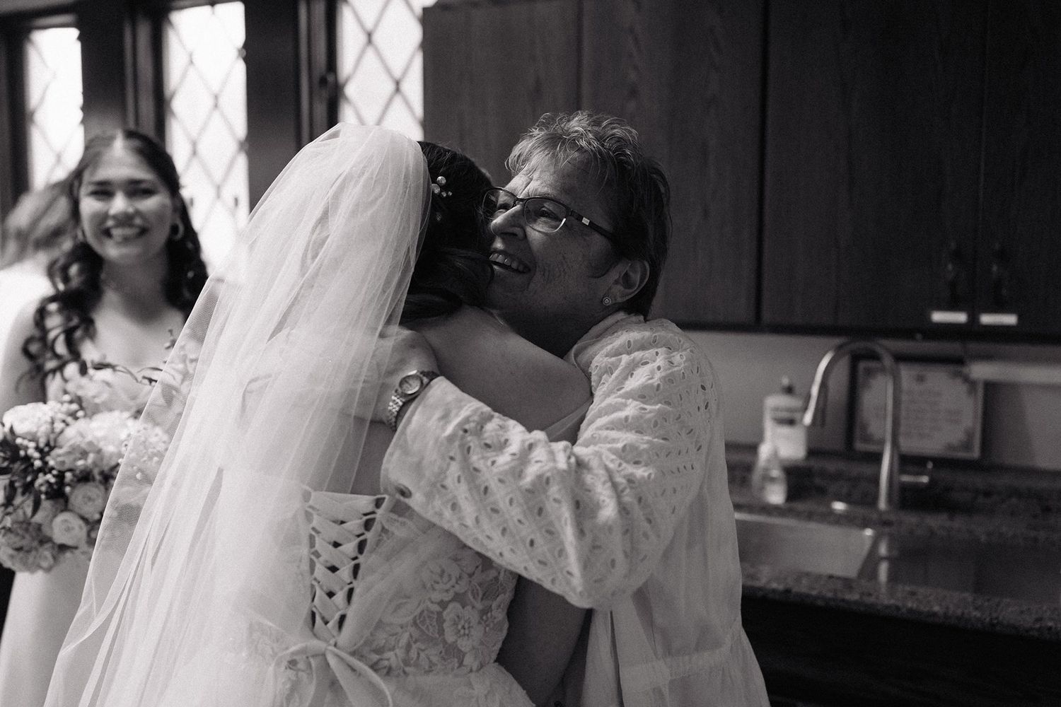 Black and white photo showing an emotional moment between two people embracing at a wedding ceremony.