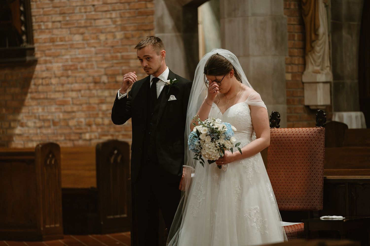 Emotional wedding ceremony moment in brick church as couple stands at altar with bridal bouquet.