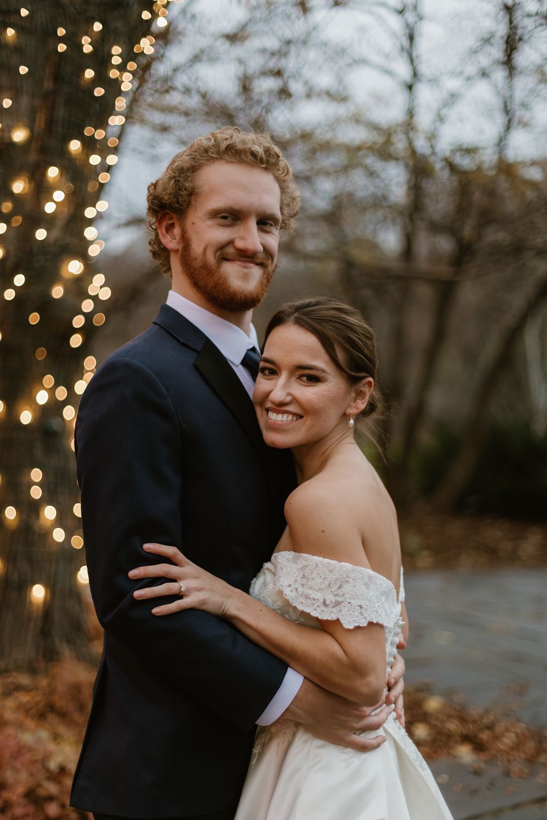 A romantic outdoor portrait at dusk with string lights twinkling in the background.