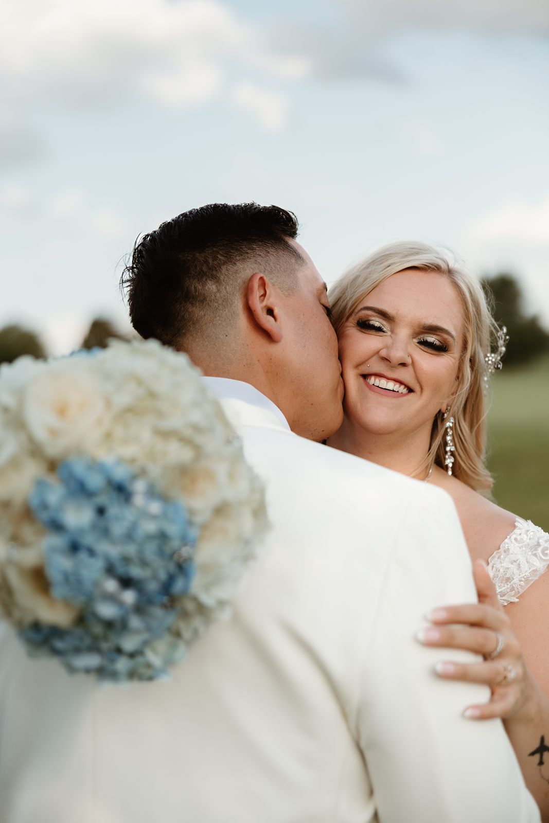 A romantic moment captured between newlyweds with a blue and white bouquet visible in the foreground.