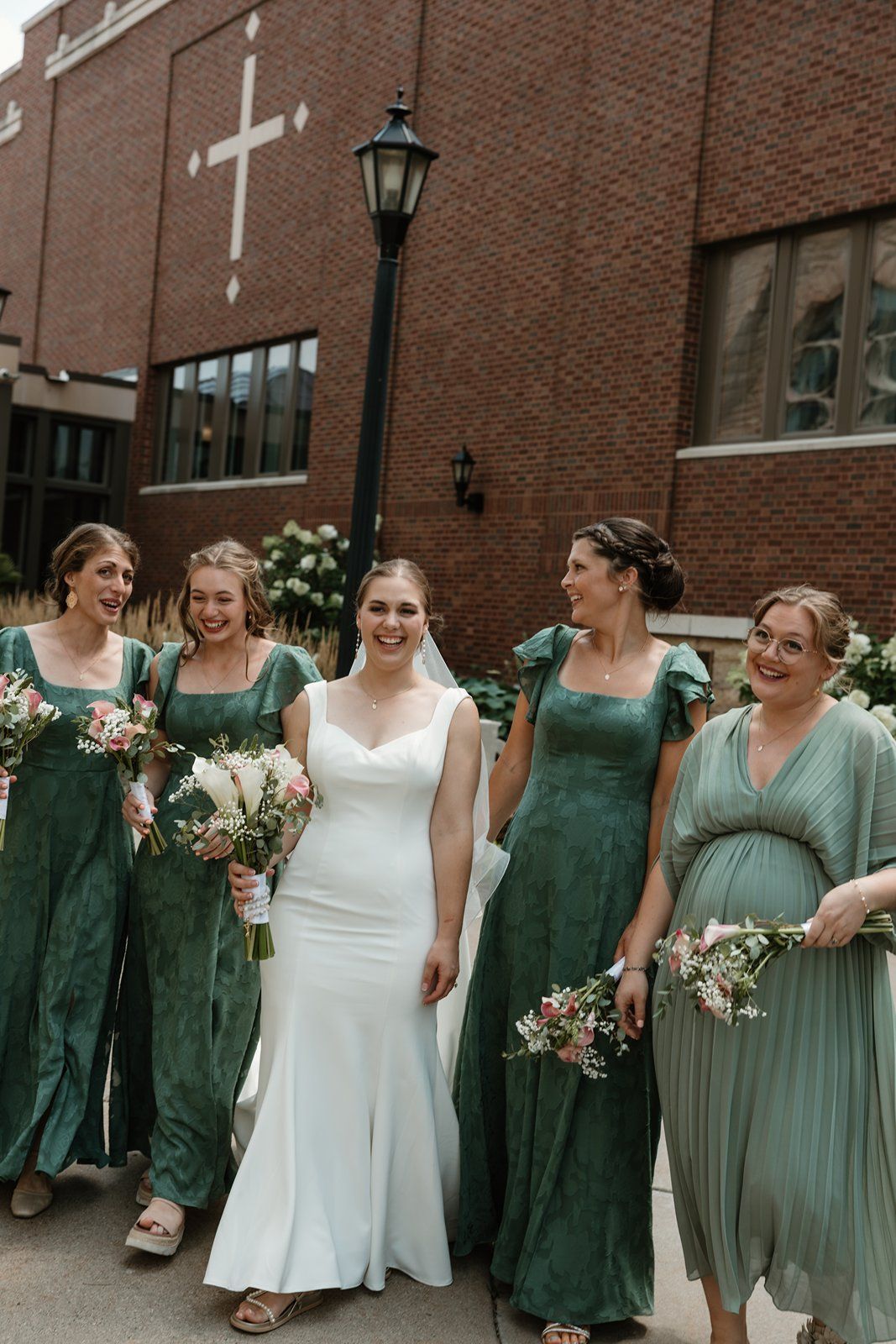 A group of bridesmaids in green dresses walk and laugh together with a bride in white during a wedding celebration.