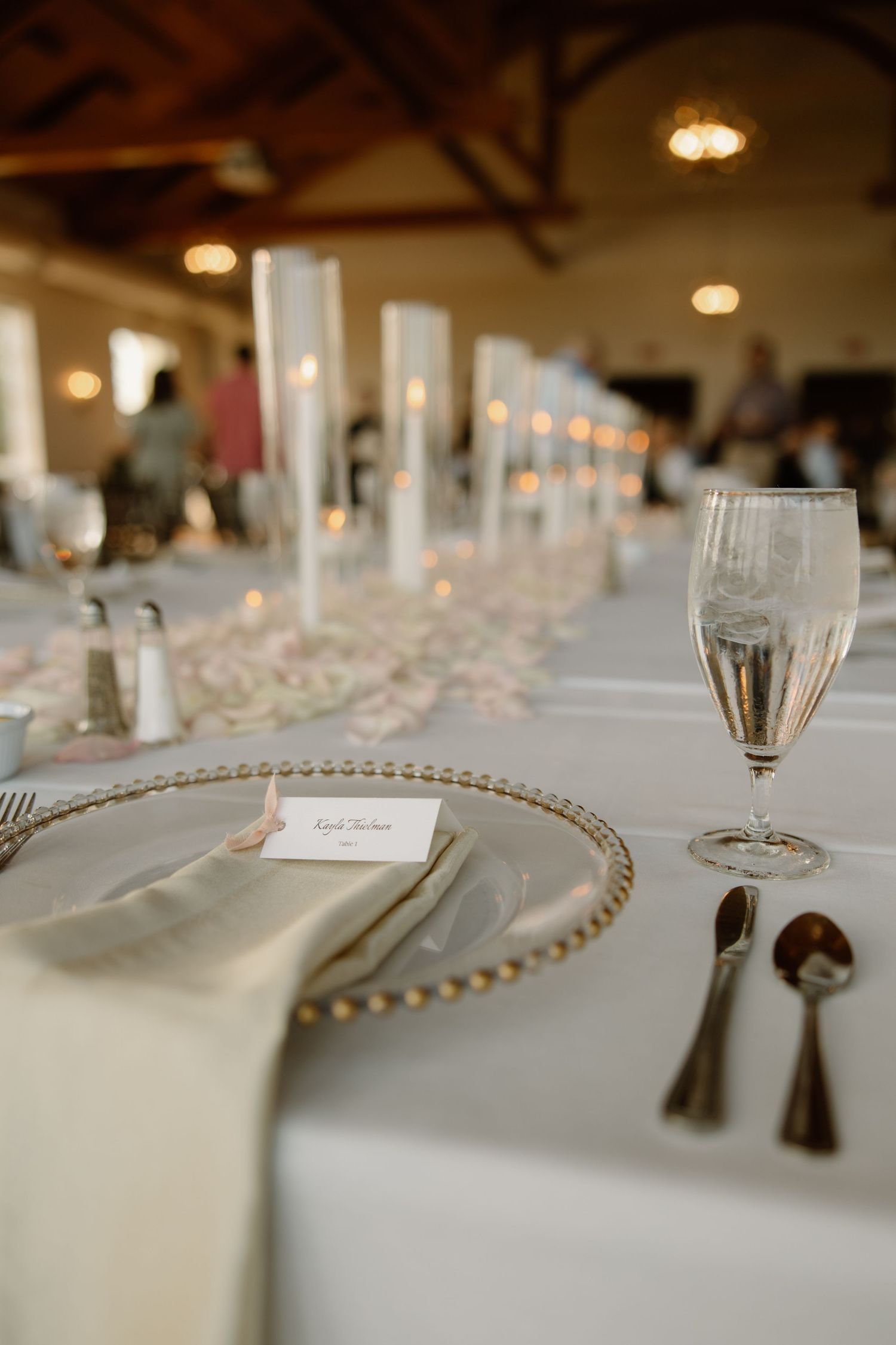 Elegant wedding table setting with beaded charger plate, champagne glass and soft candlelight in reception venue.