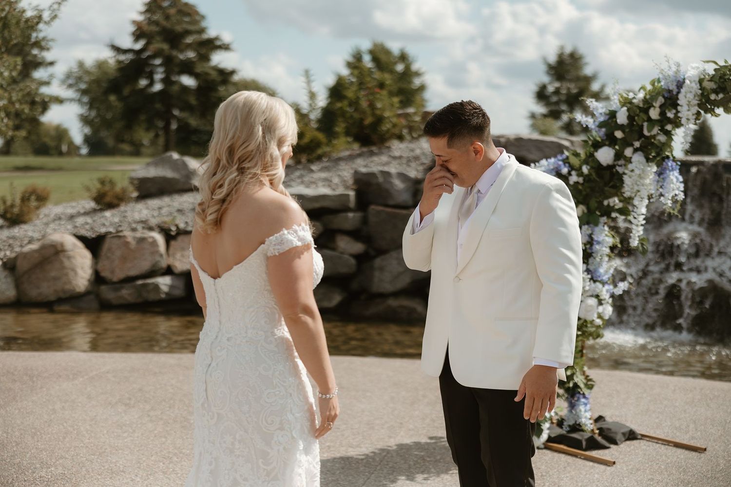 A touching first look wedding moment near a decorative stone water feature.